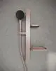 Brausekombination von Ideal Standard mit runder Handbrause, Wandhalterung und zwei Ablagen in Rosé, montiert an einer hellen, strukturierten Wand.
